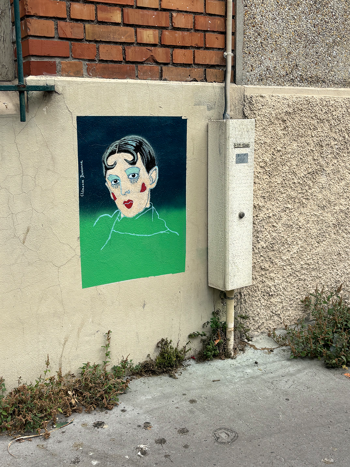 Portrait de Claude Cahun peint sur un mur de rue, au-dessus du trottoir, à côté d'un boîtier électrique