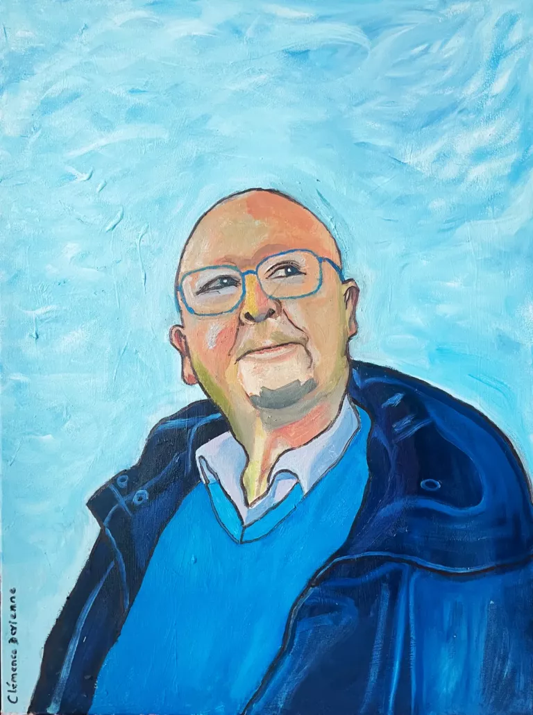 Portrait de M. Rabier : homme chauve aux lunettes bleues, veste bleu marine, sur un fond de ciel bleu