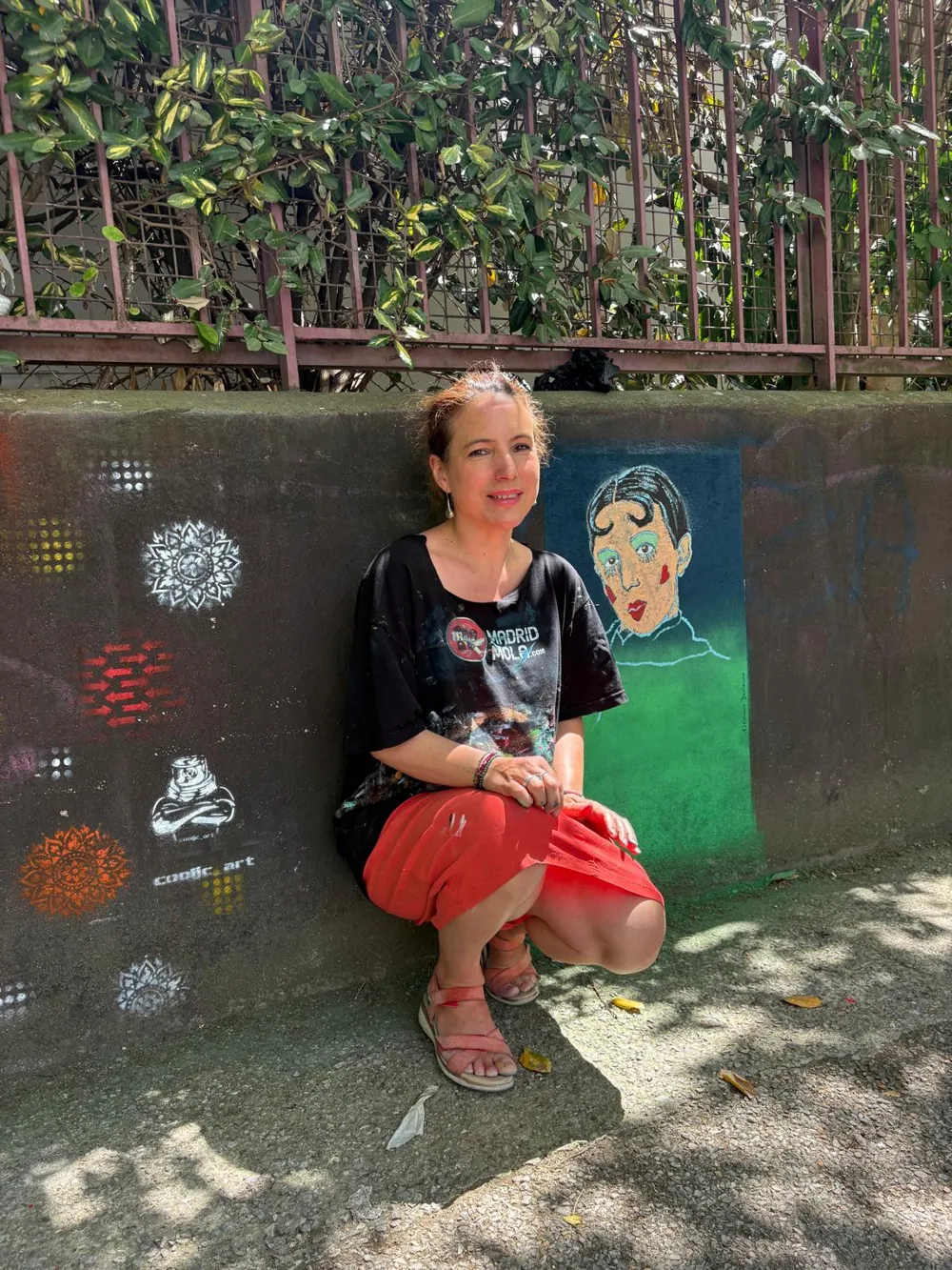 Clémence Devienne, accroupie dans une rue du 14e arrondissement de Paris, devant son portrait de Claude Cahun peint sur un mur, entouré de motifs au pochoir